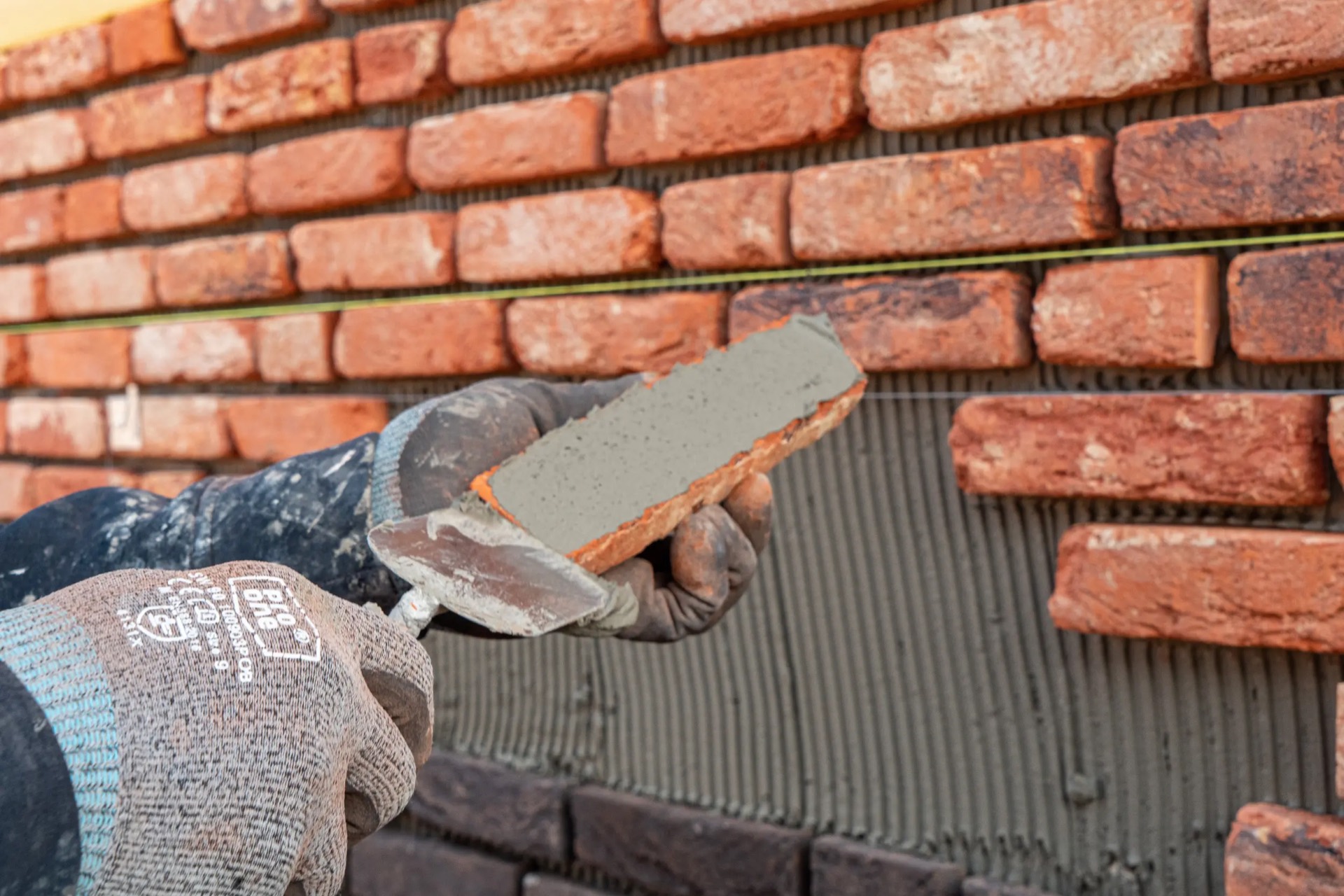 Vakman van IBS Afbouw brengt een steenstrip aan op een gevel