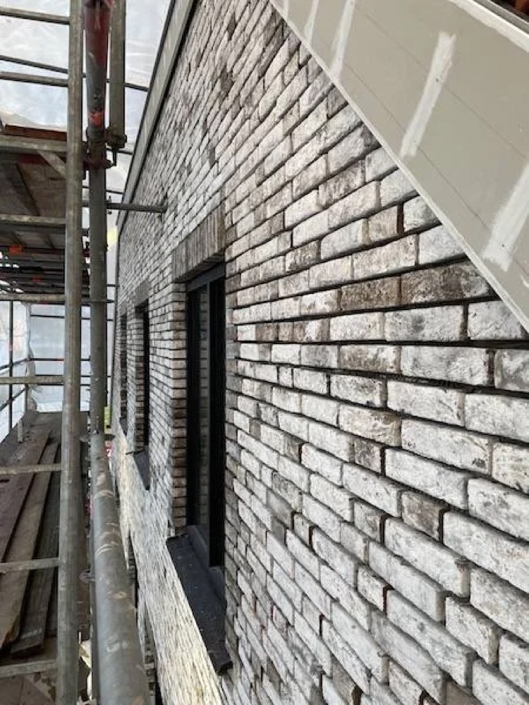 Vakman van IBS Afbouw brengt steenstrips aan op een betonnen ondergrond in Alkmaar